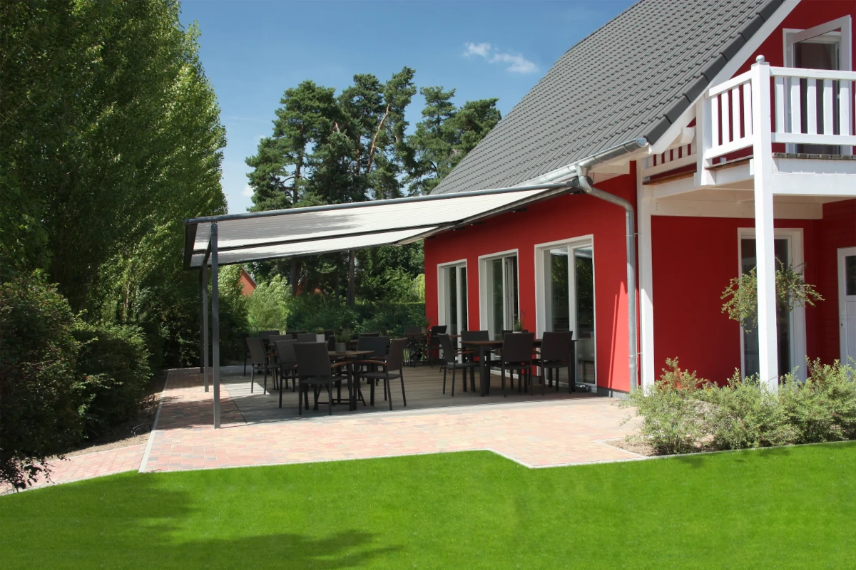 Rotes Ferienhaus mit Terrasse, Gartenmöbeln und Sonnenmarkise im Garten